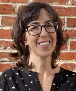 Anne-Kupinski-woman with shoulder length brown hair, glasses, and a black pattern shirt