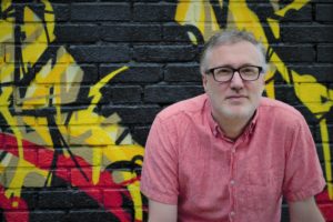 Vincent Fumo - man with short grey hair, black glasses, pink shirt in front of a mural